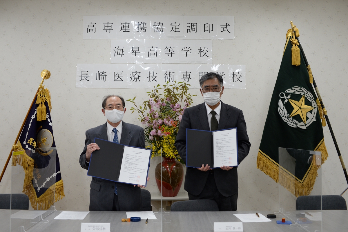 署名した協定書を掲げる医技専の分部哲明校長（左）と海星の武川眞一郎校長（右）